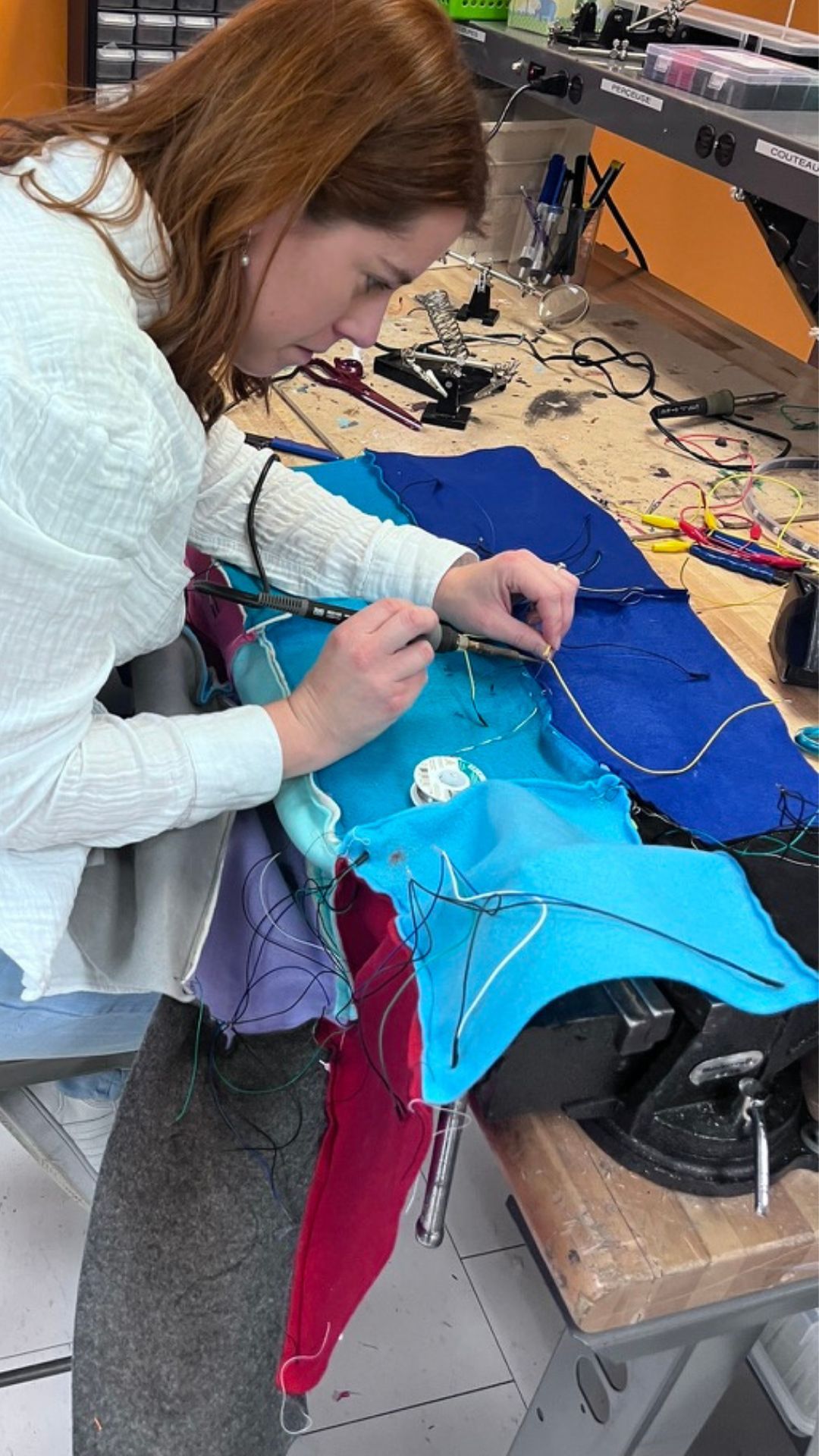 Woman working on a project on a work bench using a soldering iron, and some wire on a piece of fabric